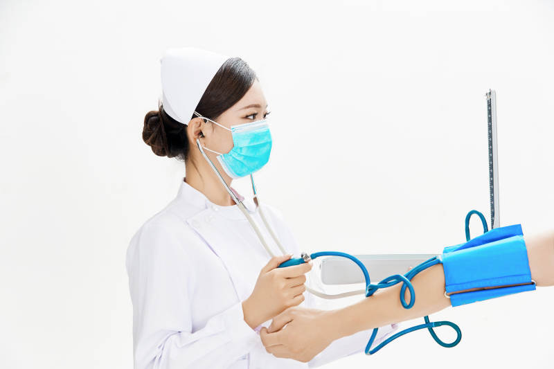 白色背景下手持血压计为患者测量血压的护士图片