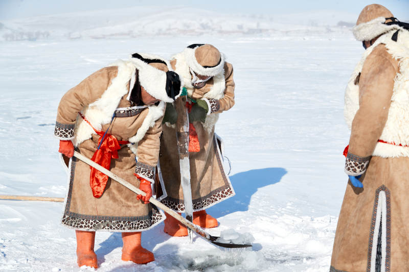 寒冷的冬季在冰冻的湖面上凿冰捕鱼的人们图片