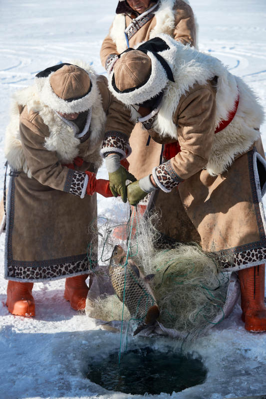 寒冷的冬季在冰冻的湖面上凿冰捕鱼的人们图片