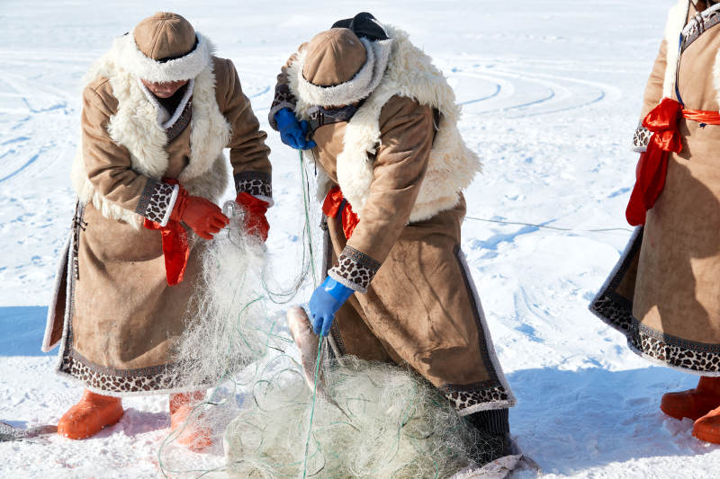 寒冷的冬季在冰冻的湖面上凿冰捕鱼的人们图片