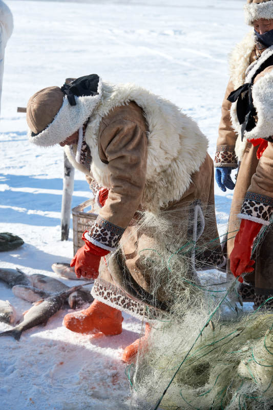 寒冷的冬季在冰冻的湖面上凿冰捕鱼的人们图片