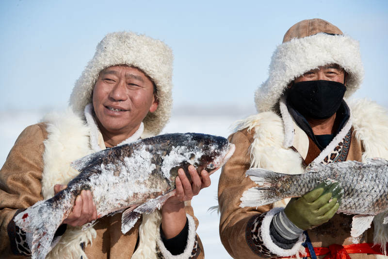 寒冷的冬季在冰冻的湖面上凿冰捕鱼的人们图片