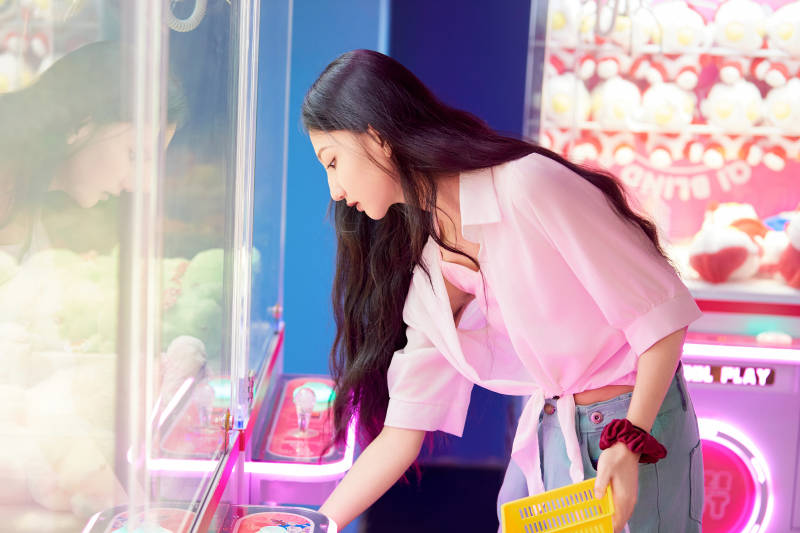 在电子游戏娱乐城玩抓娃娃机的时尚少女图片