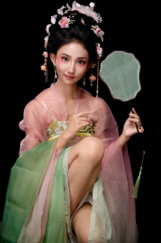 身着唐代簪花仕女服手持轻扇的坐姿女性图片