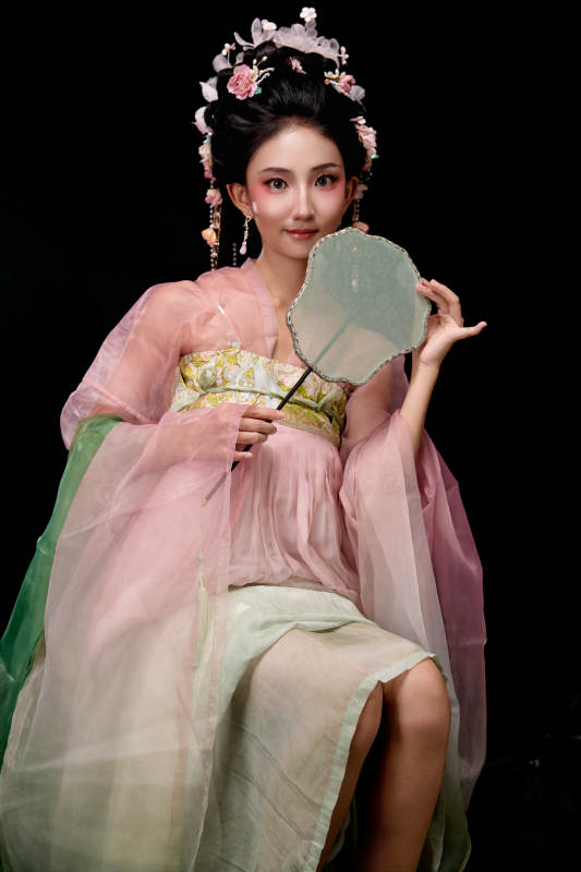 身着唐代簪花仕女服手持轻扇的坐姿女性图片