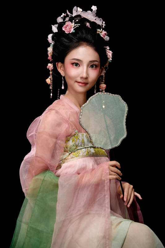 身着唐代簪花仕女服手持轻扇的坐姿女性图片