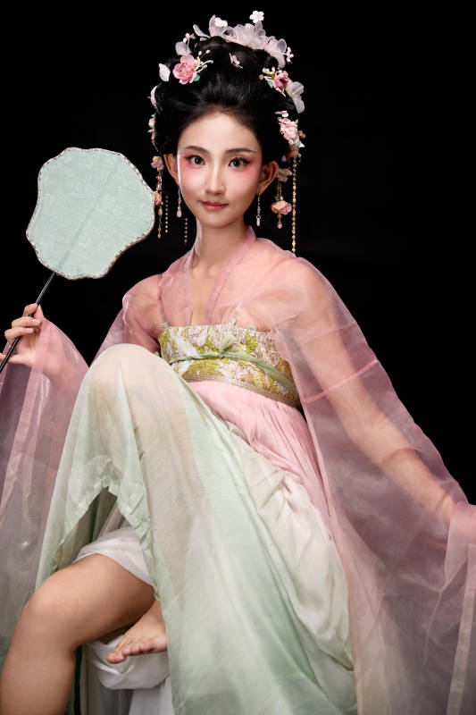 身着唐代簪花仕女服手持轻扇的坐姿女性图片