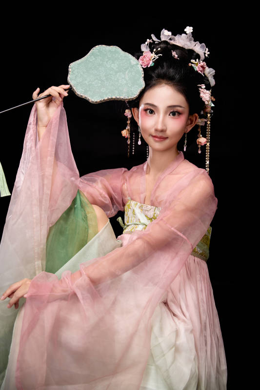 身着唐代簪花仕女服手持轻扇的坐姿女性图片