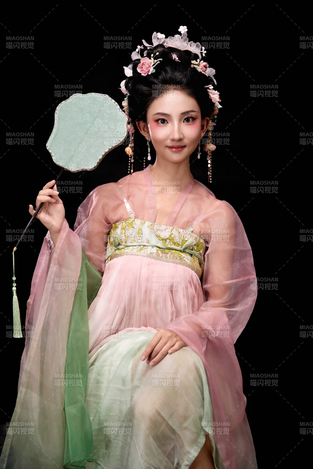 身着唐代簪花仕女服手持轻扇的坐姿女性图片