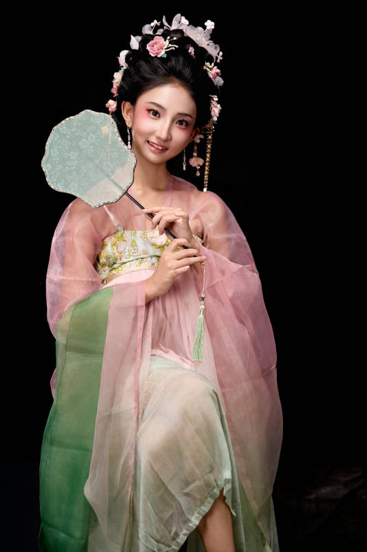 身着唐代簪花仕女服手持轻扇的坐姿女性图片