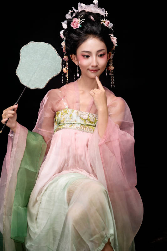 身着唐代簪花仕女服手持轻扇的坐姿女性图片