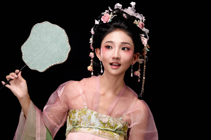 身着唐代簪花仕女服手持轻扇的坐姿女性图片