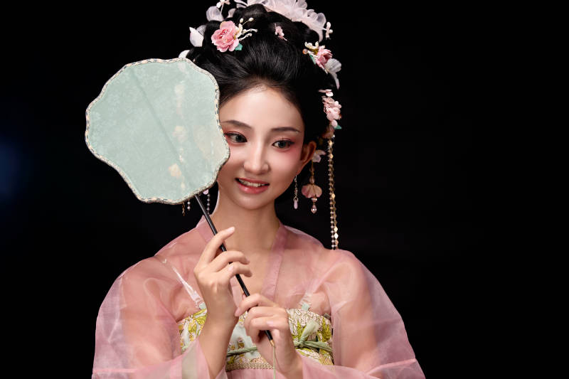 身着唐代簪花仕女服手持轻扇的坐姿女性图片