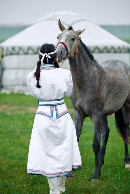 草原上穿着蒙古族服饰牵着马匹的亚洲美女图片