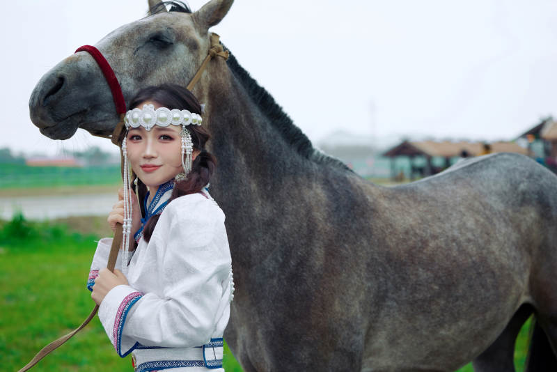 草原上穿着蒙古族服饰牵着马匹的亚洲美女图片