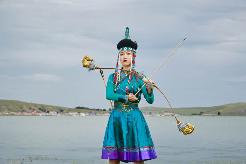 草原湖畔身穿蒙古族饰手持弓箭的蒙族少女图片