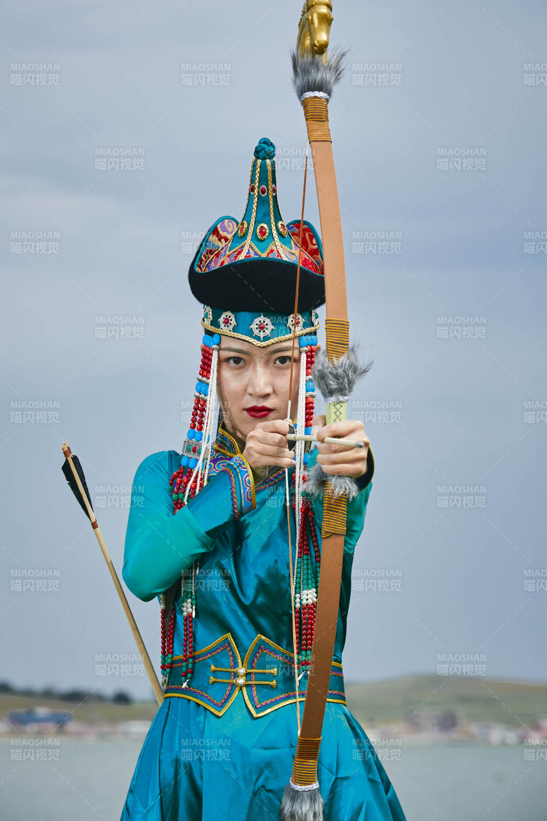 草原湖畔身穿蒙古族饰手持弓箭的蒙族少女图片
