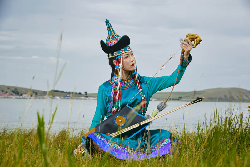 草原湖畔身穿蒙古族饰手持弓箭的蒙族少女图片