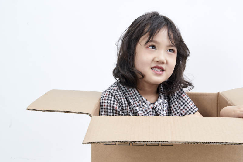 躲在纸箱中玩耍的调皮可爱亚洲小女孩儿童图片