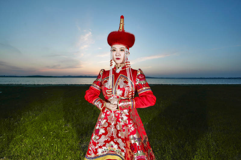 晚霞的草原湖畔穿蒙古族传统服饰的年轻女性图片