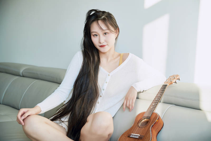 坐在沙发上弹奏尤克里里的少女图片