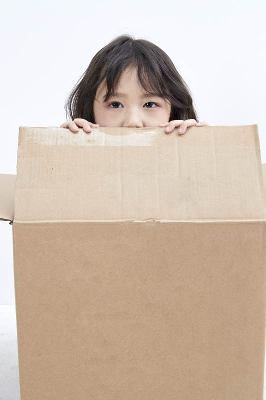 躲在纸箱中玩耍的调皮可爱亚洲小女孩儿童图片