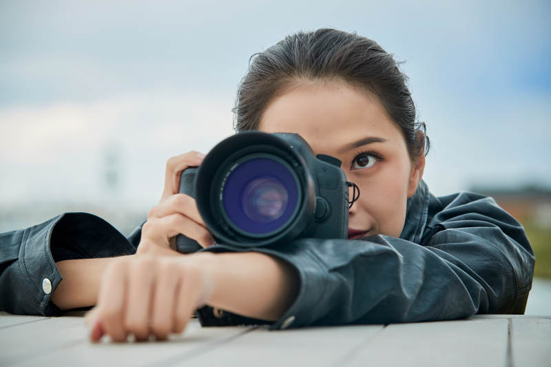 户外湖畔进行拍摄的亚洲青年女性摄影师图片