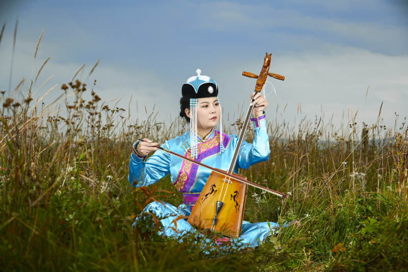 草原上穿蒙古族服饰拉马头琴的蒙族女乐手图片