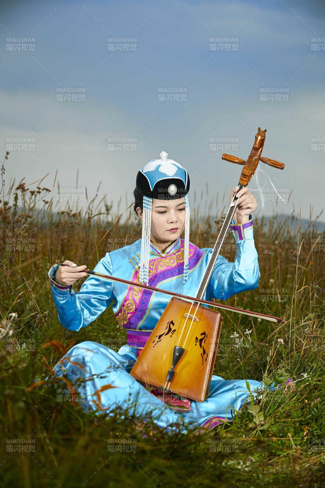 草原上穿蒙古族服饰拉马头琴的蒙族女乐手图片