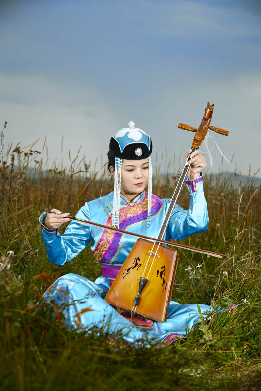 草原上穿蒙古族服饰拉马头琴的蒙族女乐手图片