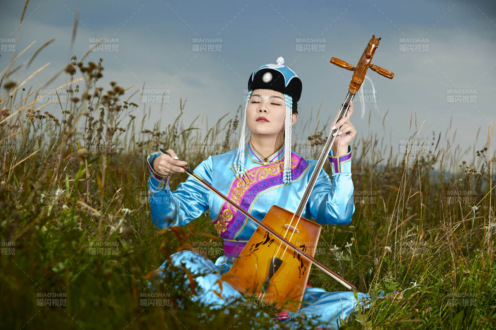 草原上穿蒙古族服饰拉马头琴的蒙族女乐手图片