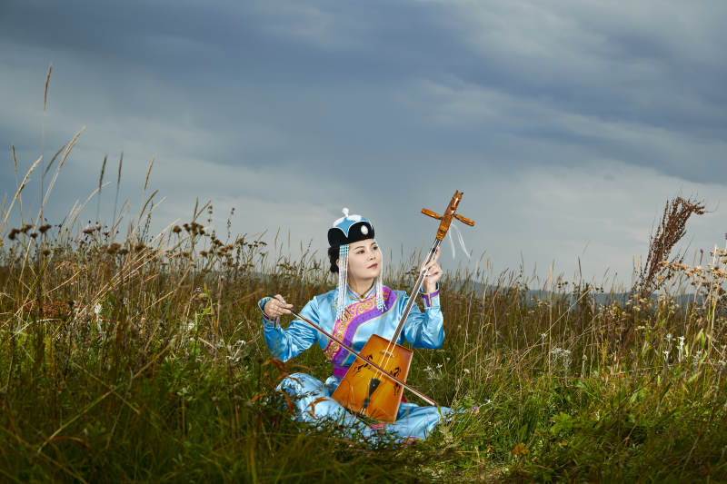 草原上穿蒙古族服饰拉马头琴的蒙族女乐手图片