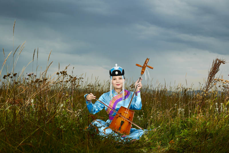 草原上穿蒙古族服饰拉马头琴的蒙族女乐手图片