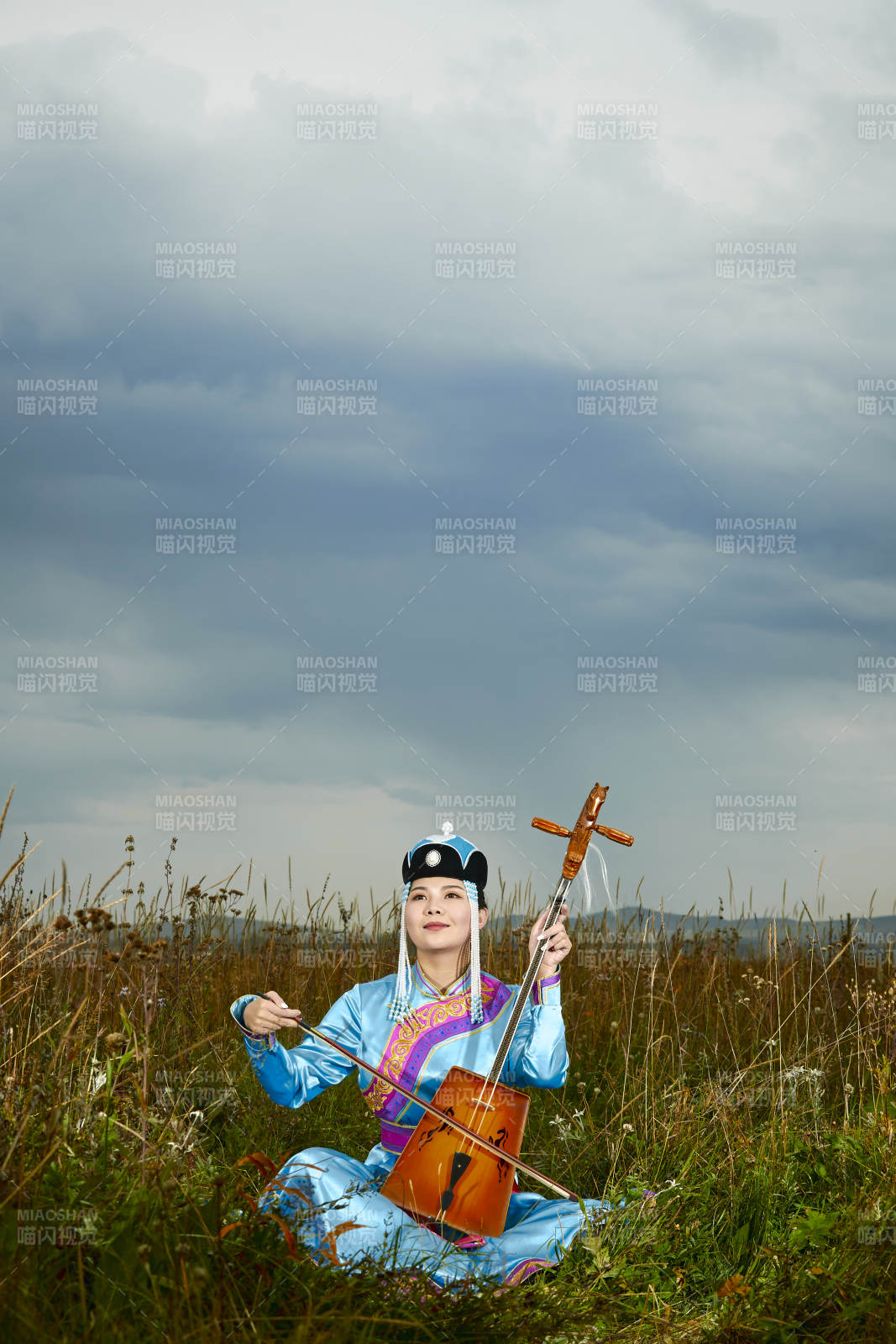 草原上穿蒙古族服饰拉马头琴的蒙族女乐手图片