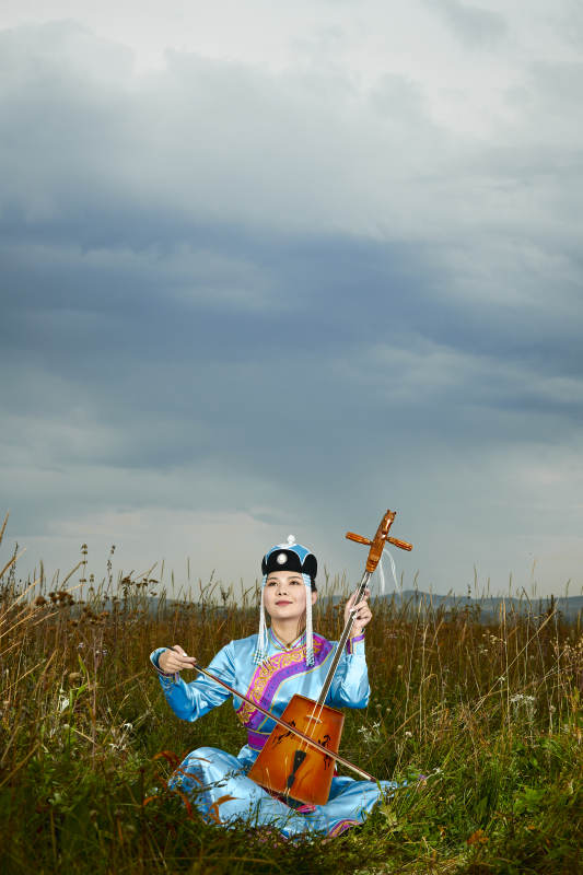 草原上穿蒙古族服饰拉马头琴的蒙族女乐手图片