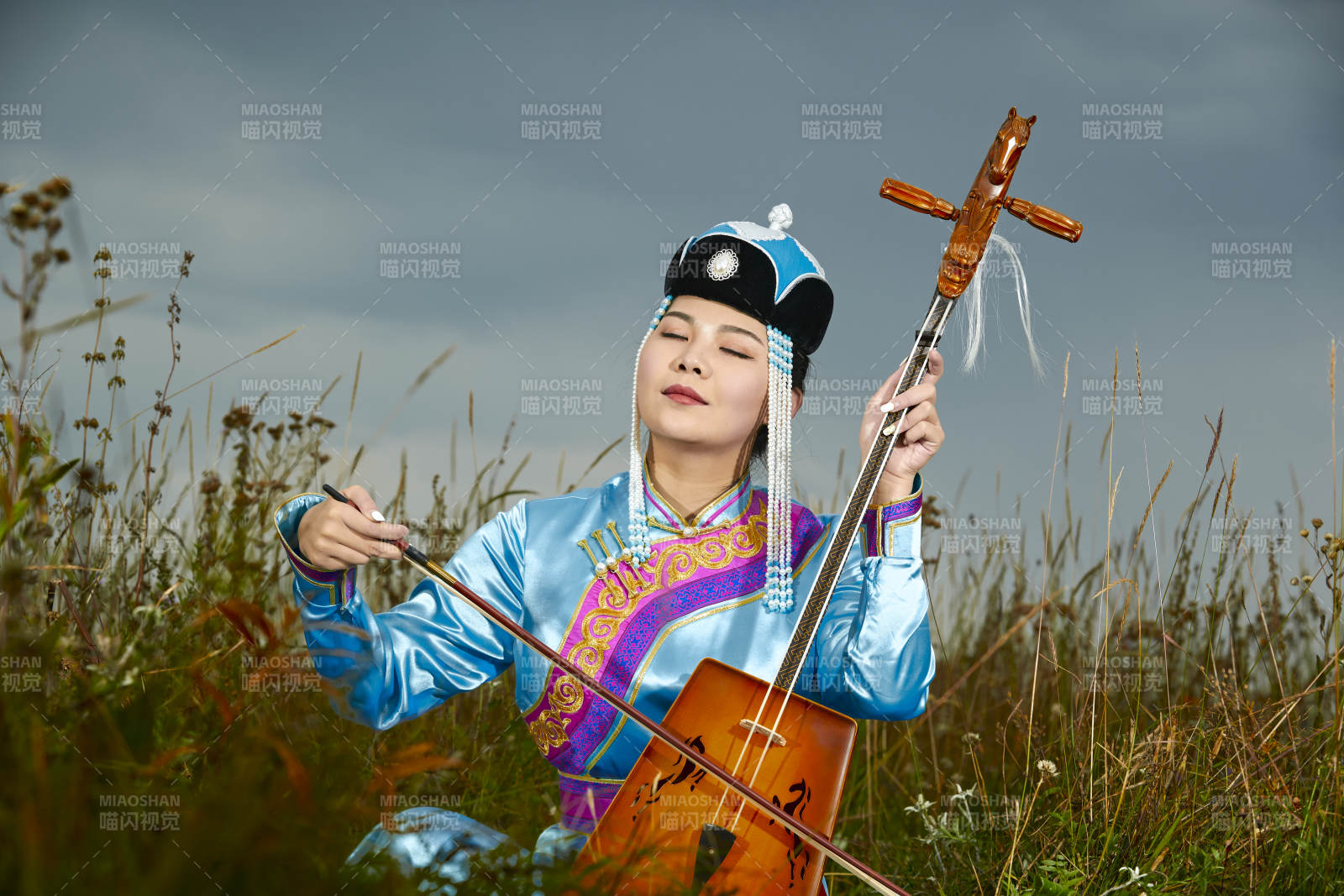 草原上穿蒙古族服饰拉马头琴的蒙族女乐手图片