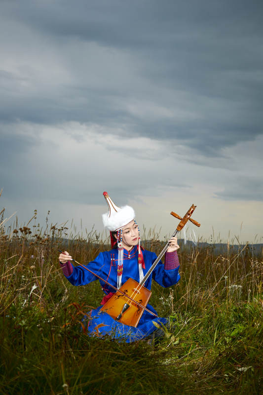 草原上穿蒙古族服饰拉马头琴的蒙族女乐手图片