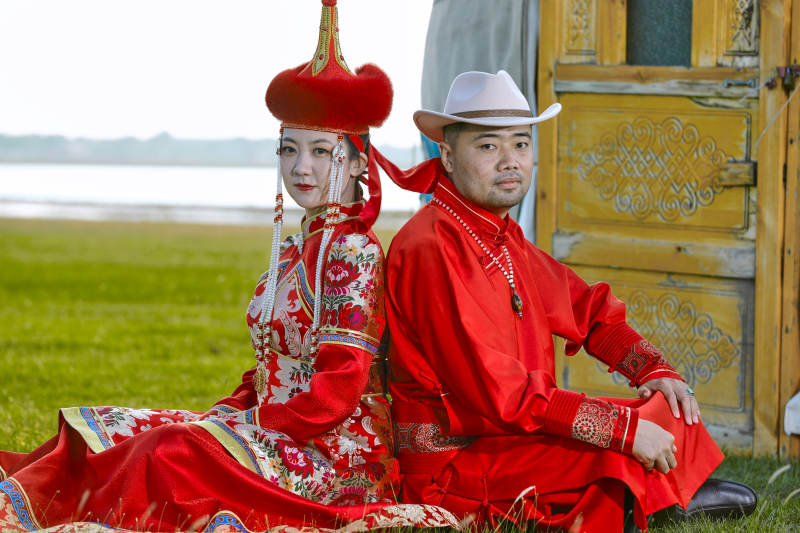 草原上蒙古包前穿蒙古族传统服饰的年轻夫妻图片
