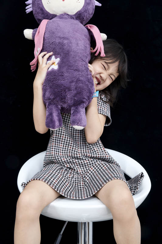 黑色背景里坐在凳子上抱着娃娃玩耍的可爱亚洲小女孩儿童图片