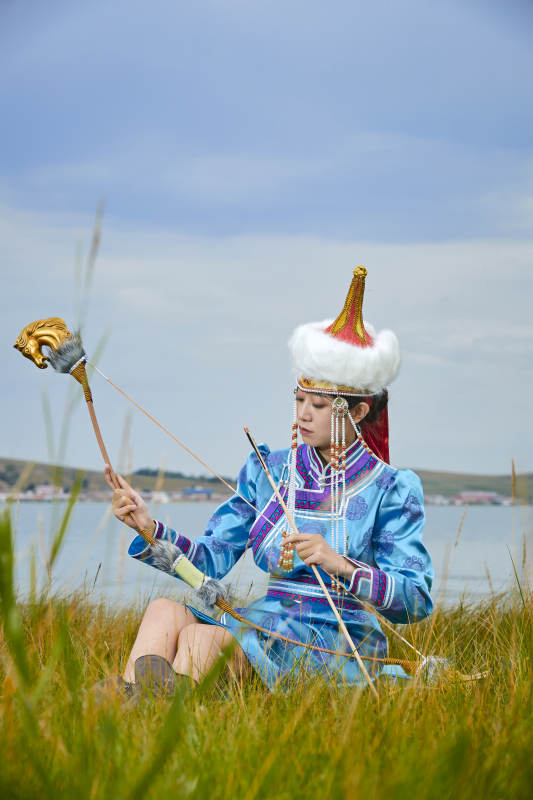 草原湖畔身穿蒙古族饰手持弓箭的蒙族少女图片