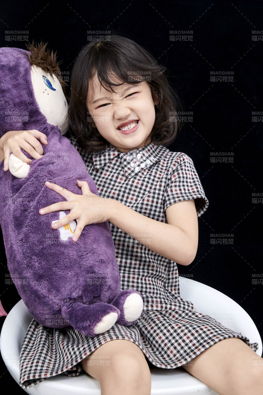 黑色背景里坐在凳子上抱着娃娃玩耍的可爱亚洲小女孩儿童图片