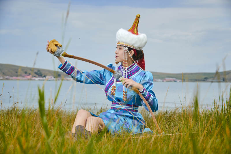 草原湖畔身穿蒙古族饰手持弓箭的蒙族少女图片