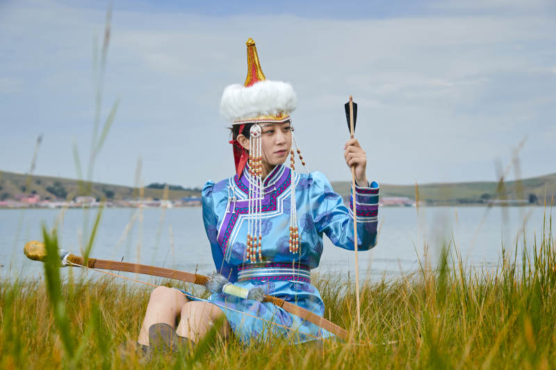 草原湖畔身穿蒙古族饰手持弓箭的蒙族少女图片