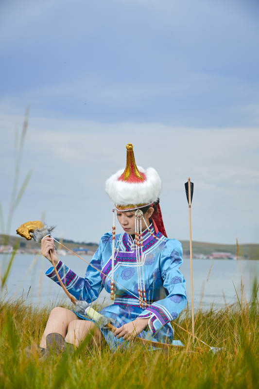 草原湖畔身穿蒙古族饰手持弓箭的蒙族少女图片