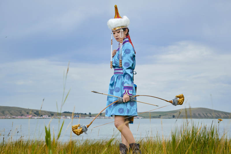 草原湖畔身穿蒙古族饰手持弓箭的蒙族少女图片