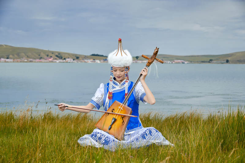 草原上穿蒙古族服饰拉马头琴的蒙族女乐手图片