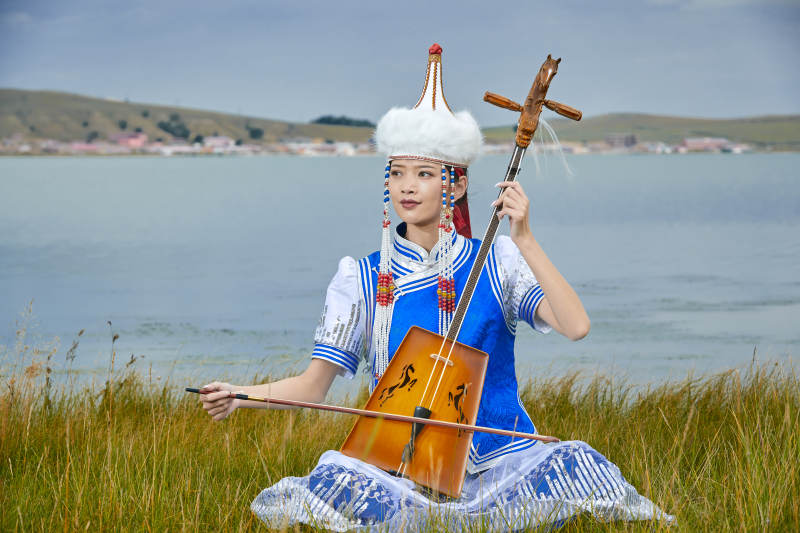 草原上穿蒙古族服饰拉马头琴的蒙族女乐手图片