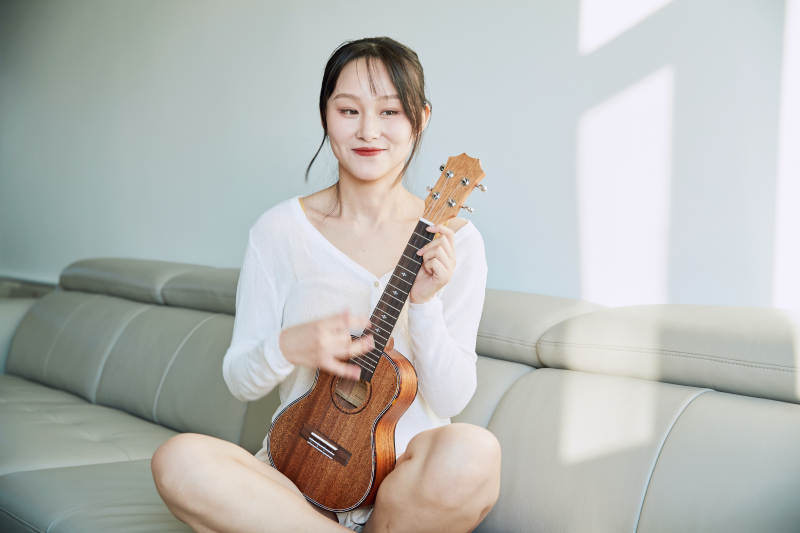 坐在沙发上弹奏尤克里里的少女图片