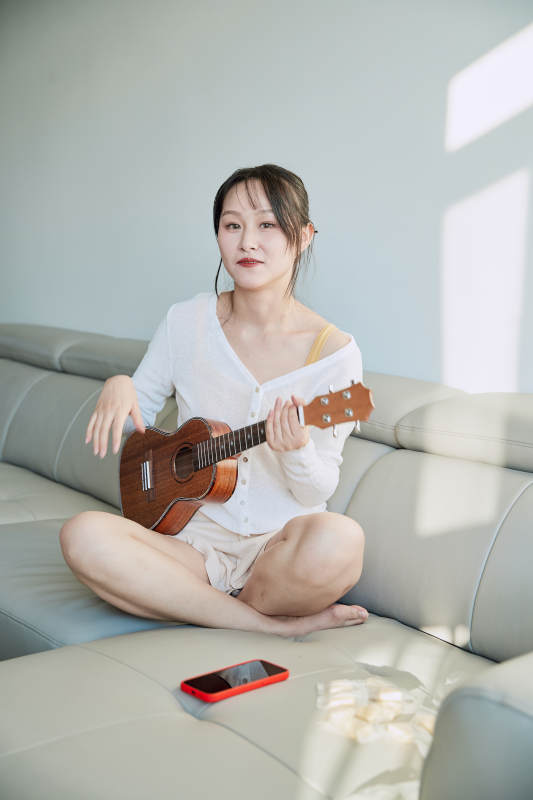 坐在沙发上弹奏尤克里里的少女图片