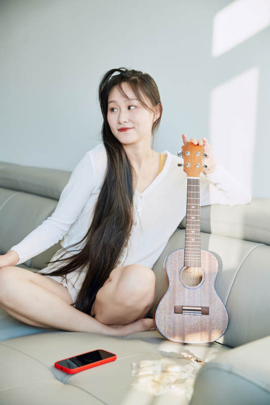坐在沙发上弹奏尤克里里的少女图片